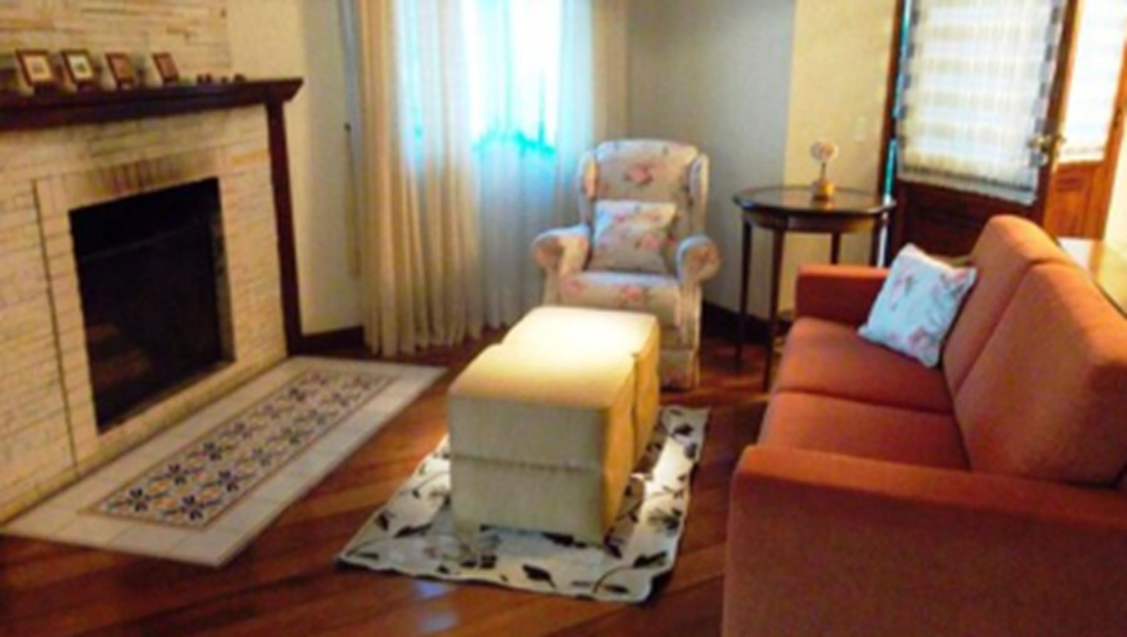 Una sala de estar con chimenea, un sillón floral, una mesita y un sofá.