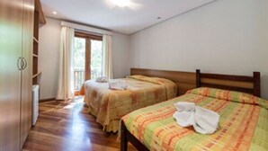 A bedroom with two beds, wooden flooring, a window with curtains, and a ceiling light. - Pousada Jóia da Serra (Campos do Jordão)