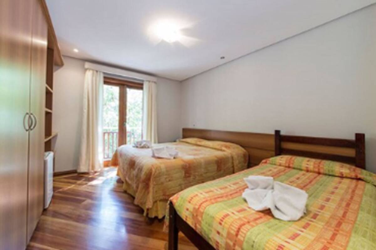 Un dormitorio con dos camas, suelo de madera, una ventana con cortinas e iluminación en el techo.