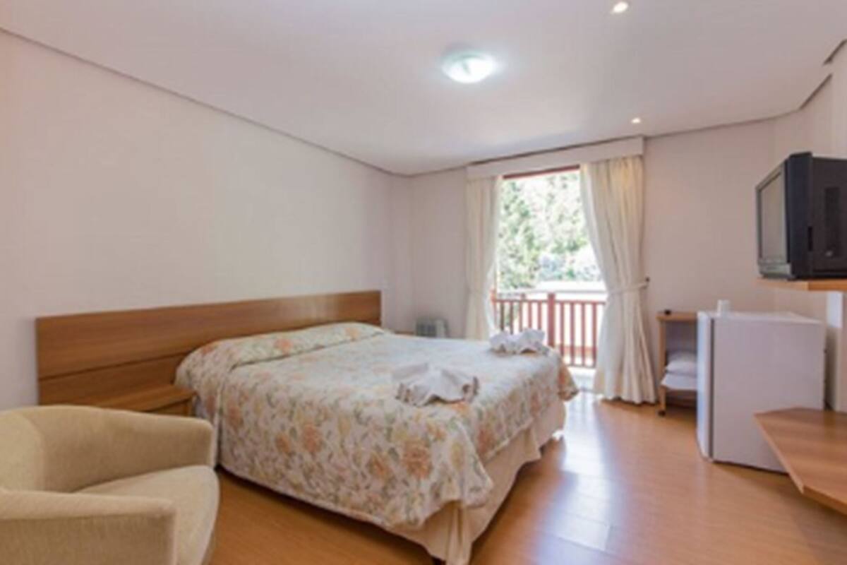Un dormitorio con cama, una silla, televisor y balcón.