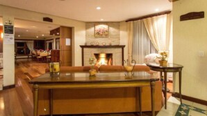 A hotel lobby with a fireplace, a dining area, and a reception desk. - Pousada Jóia da Serra (Campos do Jordão)