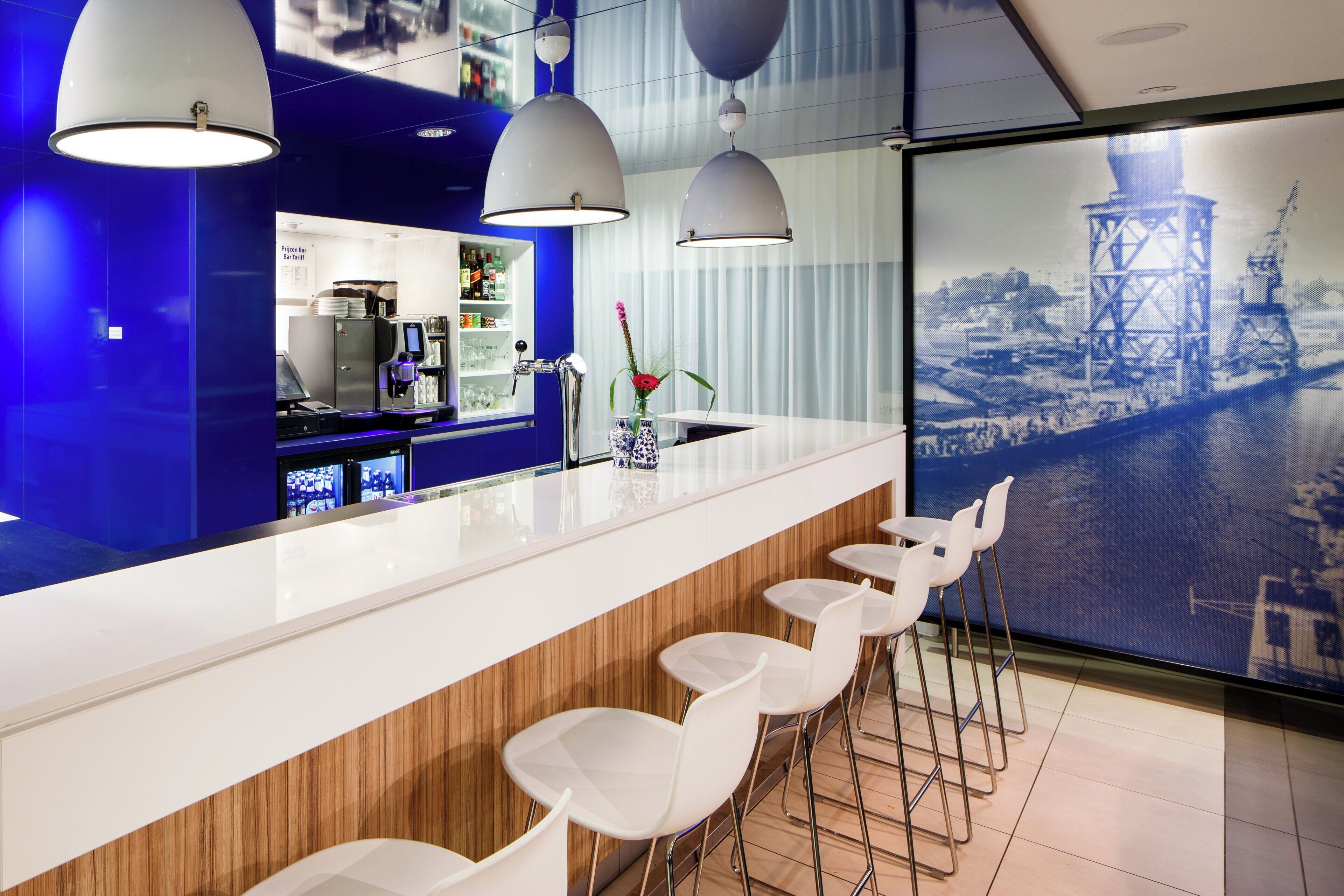 A modern bar area with a white counter, bar stools, and a cityscape view through a large window.