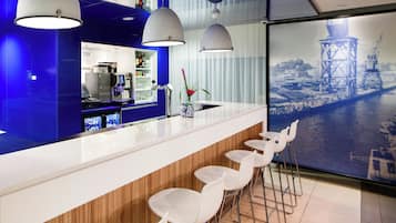 A modern bar area with a white counter, bar stools, and a cityscape view through a large window.
