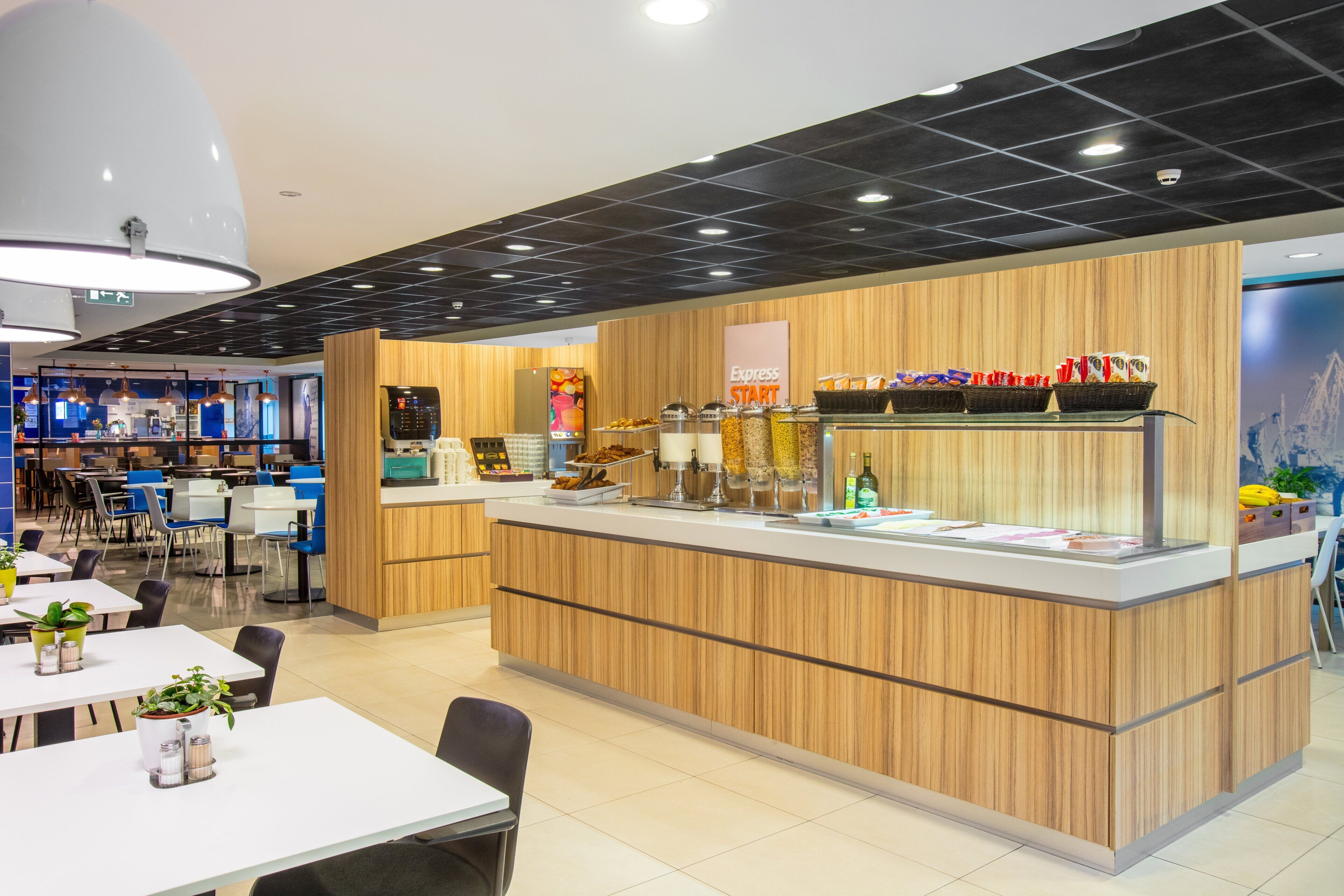 Un café moderne avec un comptoir en bois, un espace salon et un tableau des menus bien visible.