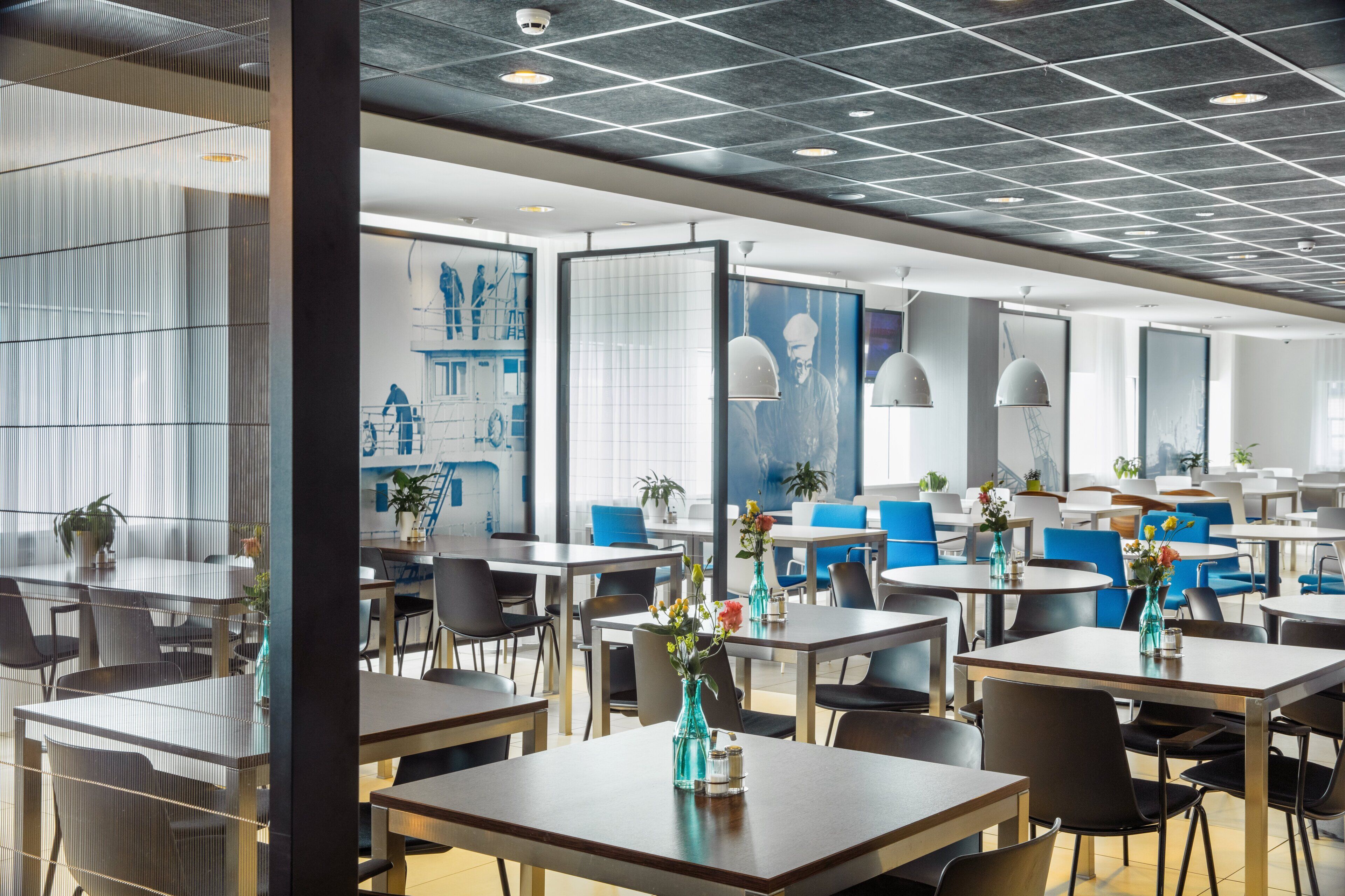 A modern dining area with tables and chairs, large windows, and artwork on the walls.