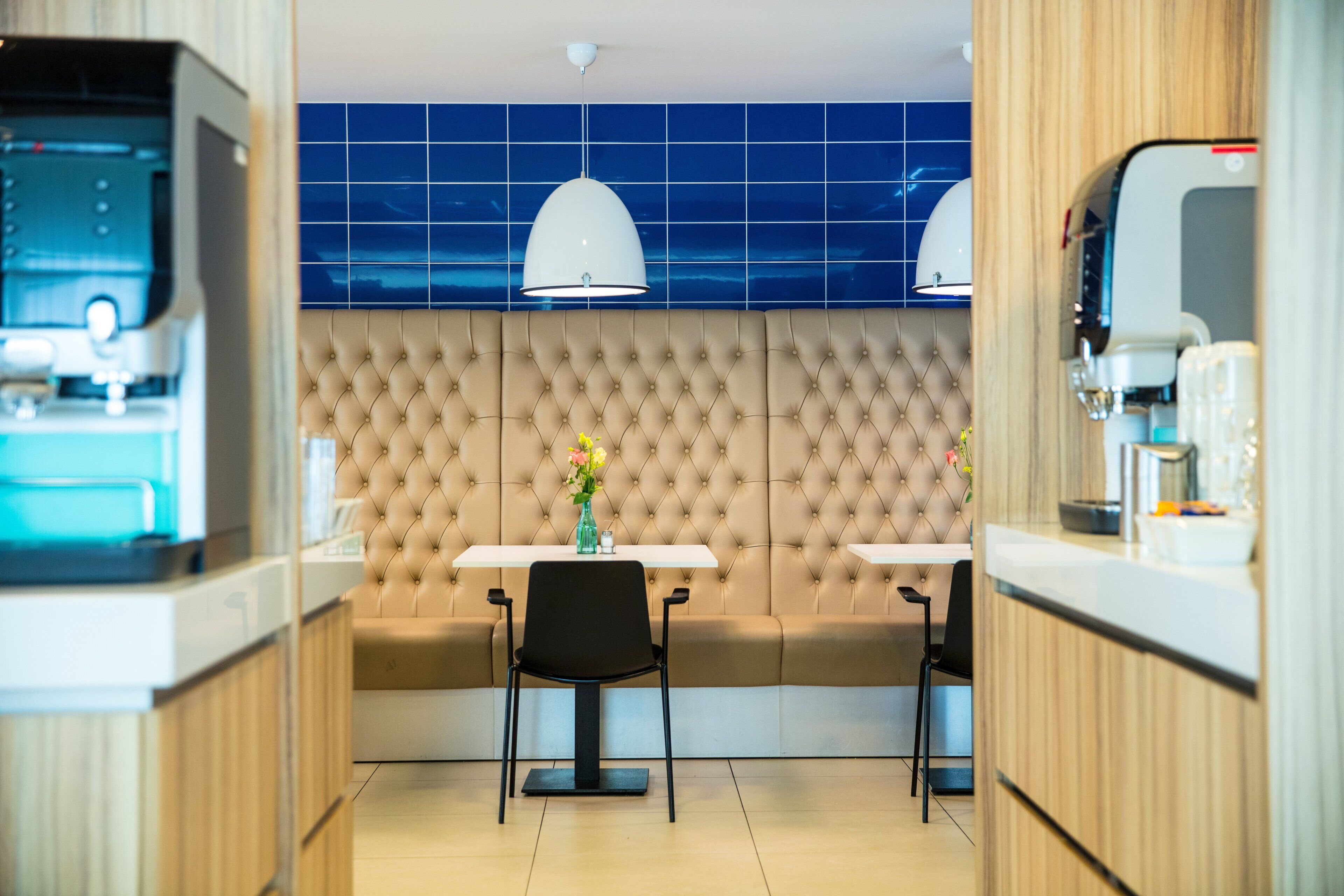 A modern kitchen with a central island, two bar stools, and a seating area with a tufted backrest.