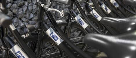 A row of bicycles with rental tags, parked against a stone wall.