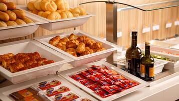 A buffet with various food items including pastries, sandwiches, and condiments.