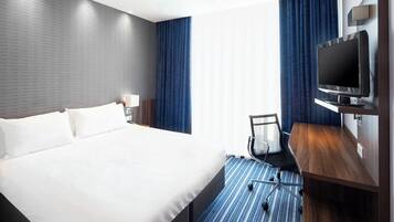 Een hotelkamer met een groot bed, een bureau met een flatscreen televisie, een stoel en een raam met gordijnen.