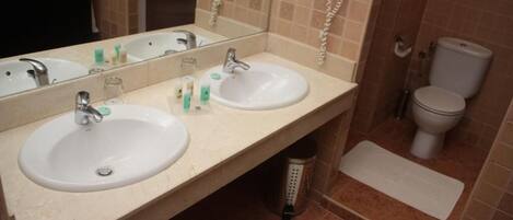 Un baño con dos lavamanos, un espejo, inodoro y zona de ducha.