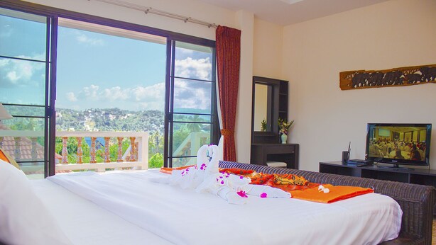 Habitación de hotel con una cama grande, televisor y balcón con vista a la ciudad.