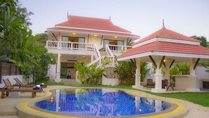 Una casa de dos pisos con piscina, un patio cubierto y un balcón.