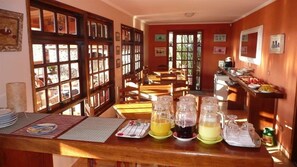 Un rincón para desayunar con mesas y sillas de madera, y un mostrador de buffet con comida y bebidas.
