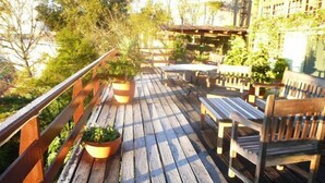 A wooden deck with outdoor furniture, including a bench and a table, surrounded by potted plants. - Pousada Benevento (Campos do Jordão)