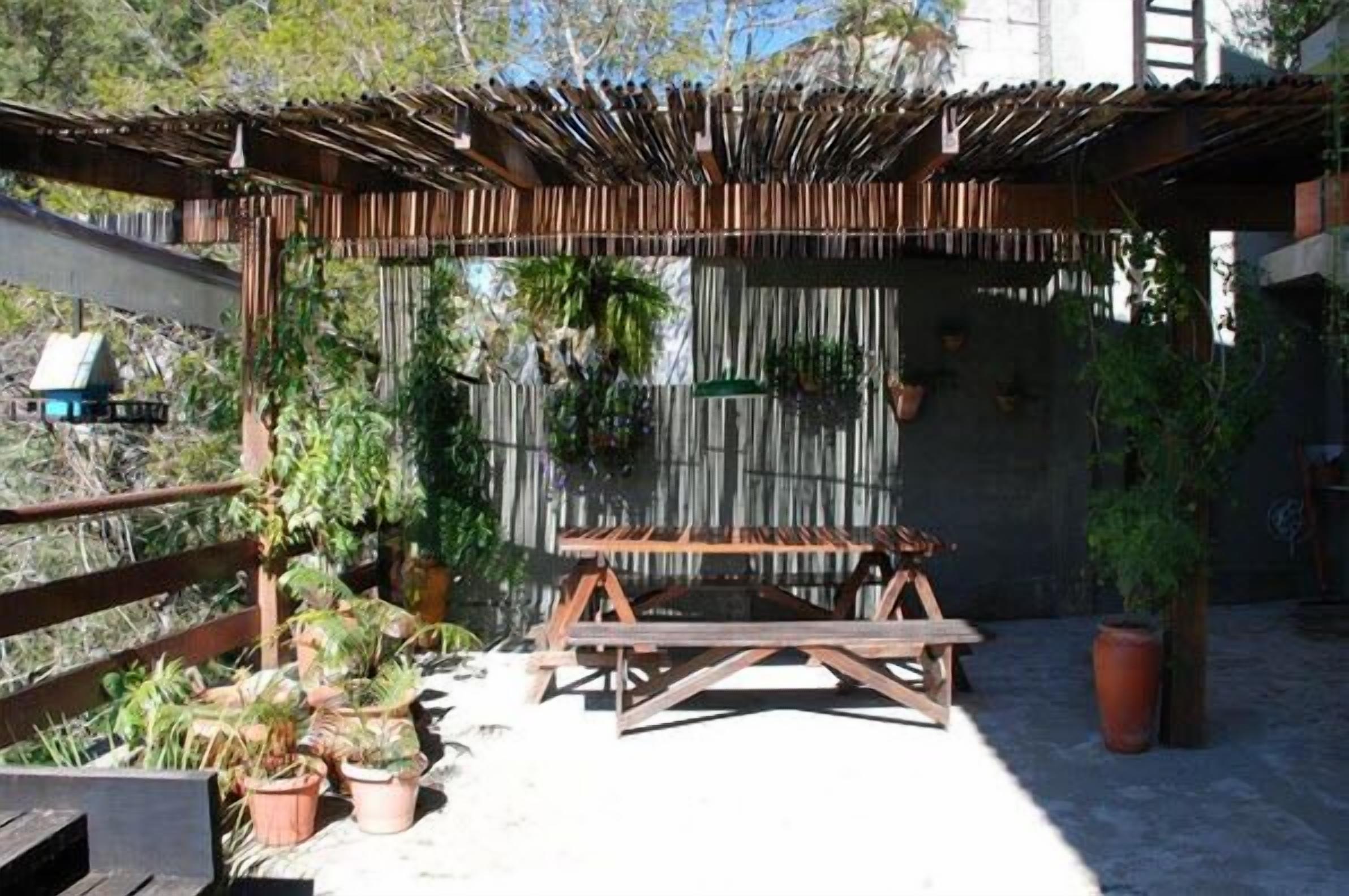An outdoor patio with a wooden pergola, a wooden table, and potted plants.