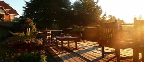 A wooden deck with a table and chairs, surrounded by potted plants and trees.