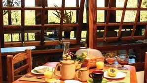 A breakfast table set with various dishes, a pitcher, and glasses, with a view of greenery through large windows. - Pousada Benevento (Campos do Jordão)