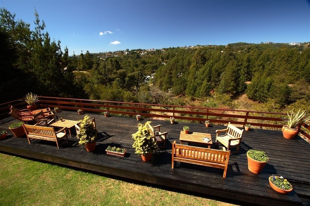 An outdoor deck with wooden furniture and potted plants, overlooking a forested area.