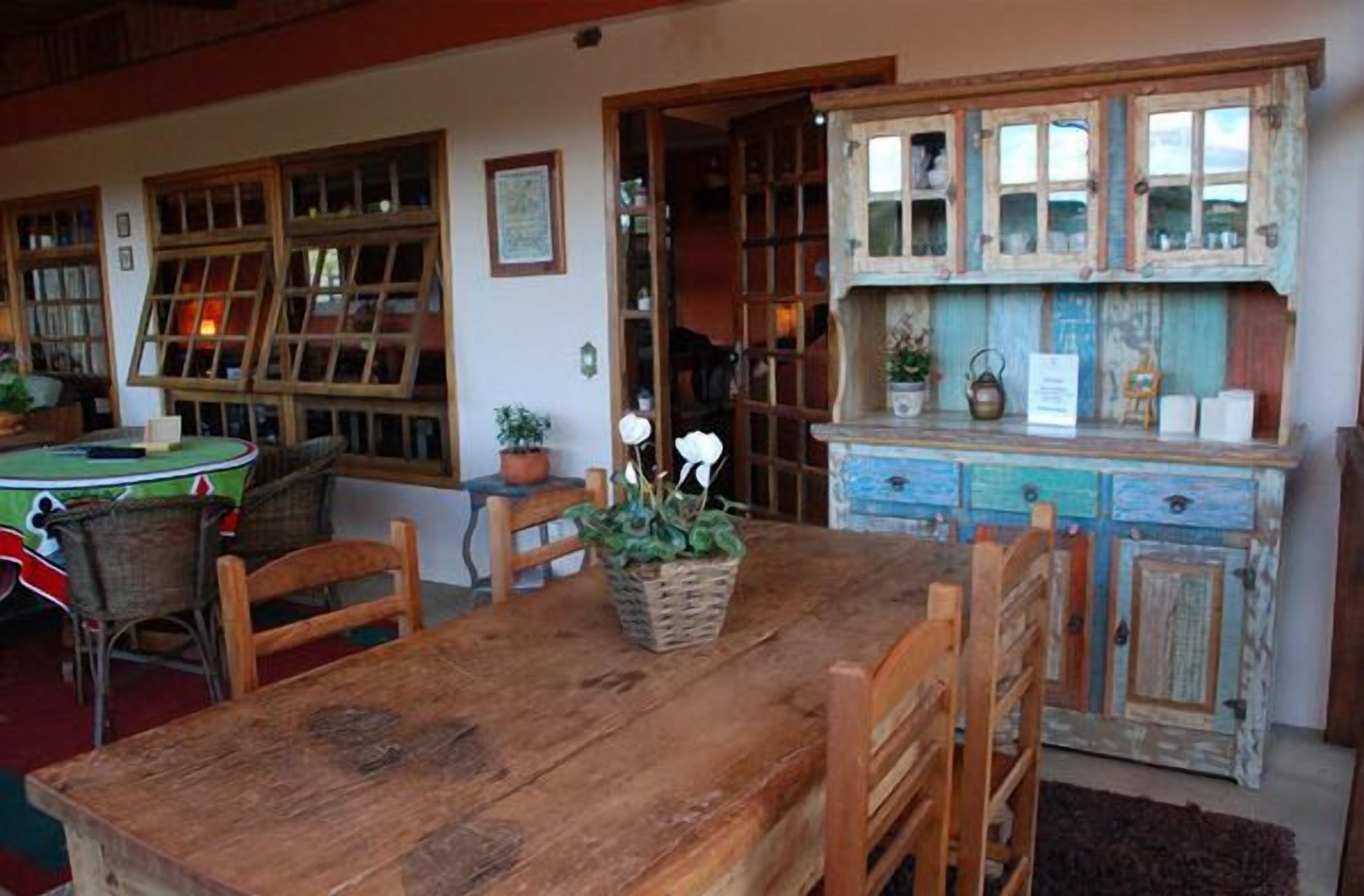 Un comedor rústico con una mesa y sillas de madera, una cesta de plantas verdes y un aparador antiguo con cajones y estantes.