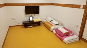 A room with a flat-screen TV mounted on the wall, a small wooden table with a lamp, and a massage table with towels. - Hyosundang (Seoul)