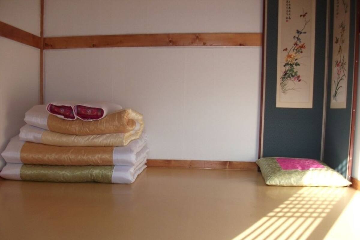 A tatami mat room with a stack of futons and a shoji screen with calligraphy.