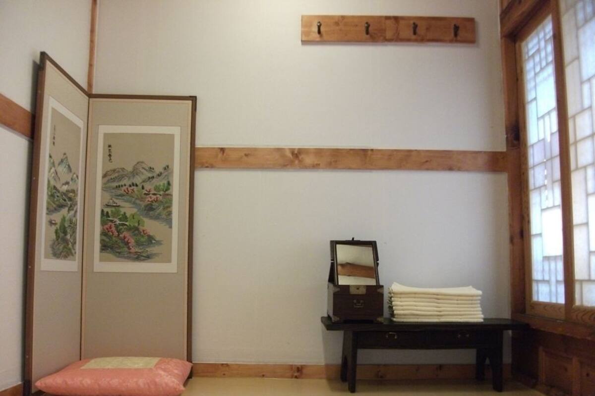 A traditional Japanese room with tatami flooring, a shoji screen with artwork, a small wooden table with a mirror, and a window with wooden frames.