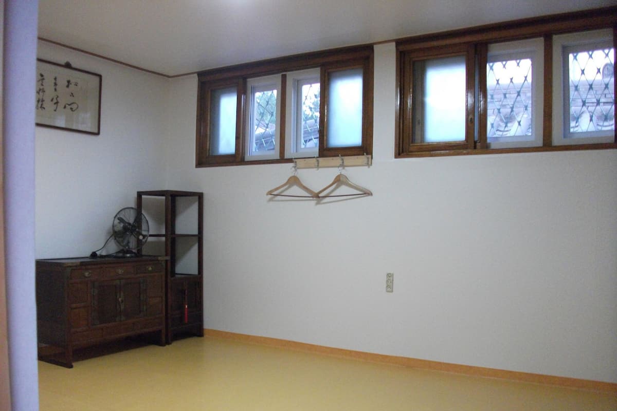 A room with a wooden cabinet, a fan, and a wall-mounted rack with hangers.