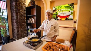 A chef preparing food in a kitchen with a stone wall, a painting of a cup of tea, and a basket of eggs. - Angkor International Hotel (Phnom Penh)