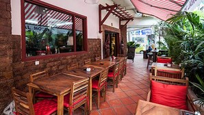 An outdoor dining area with wooden tables and chairs, a red and white striped awning, and potted plants. - Angkor International Hotel (Phnom Penh)