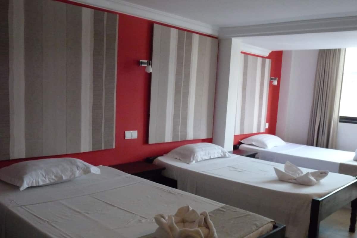 Hotellihuone, jossa on kaksi erillistä sänkyä, punainen tehosteseinä ja ikkuna, jossa on verhot.