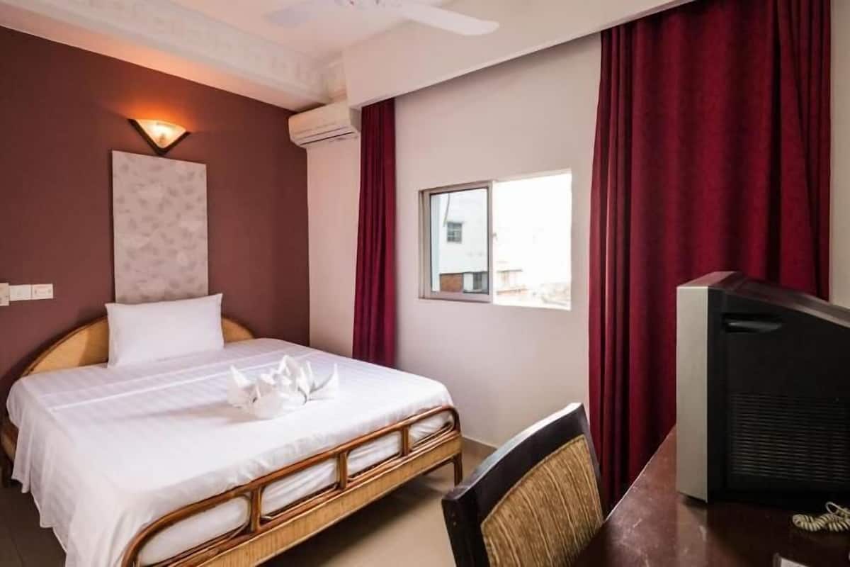 Hotellihuone, jossa on sänky, kirjoituspöytä, jossa on puhelin, televisio ja ikkuna, jossa on verhot.
