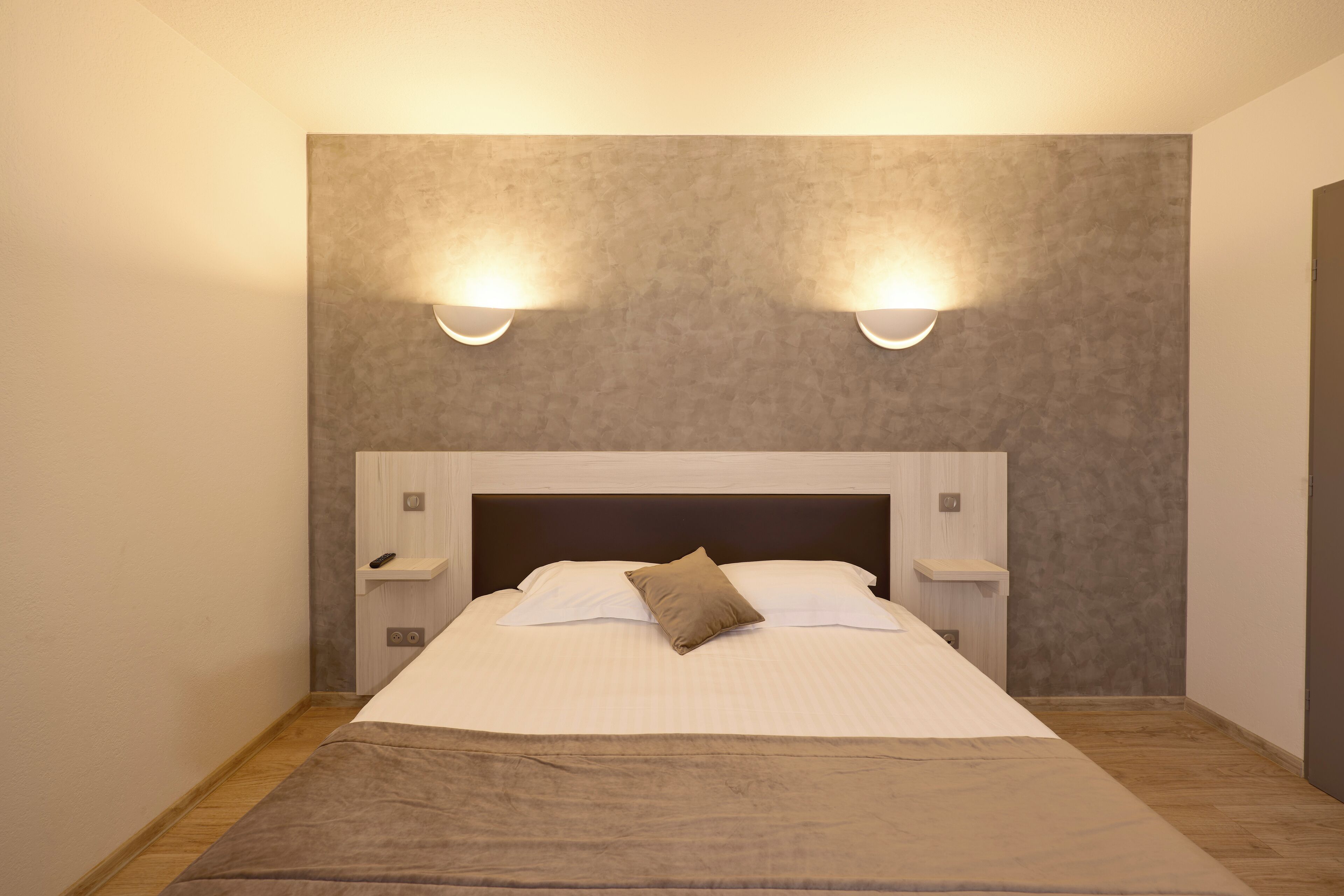 A neatly made bed with a headboard, two bedside tables, and wall-mounted lighting.