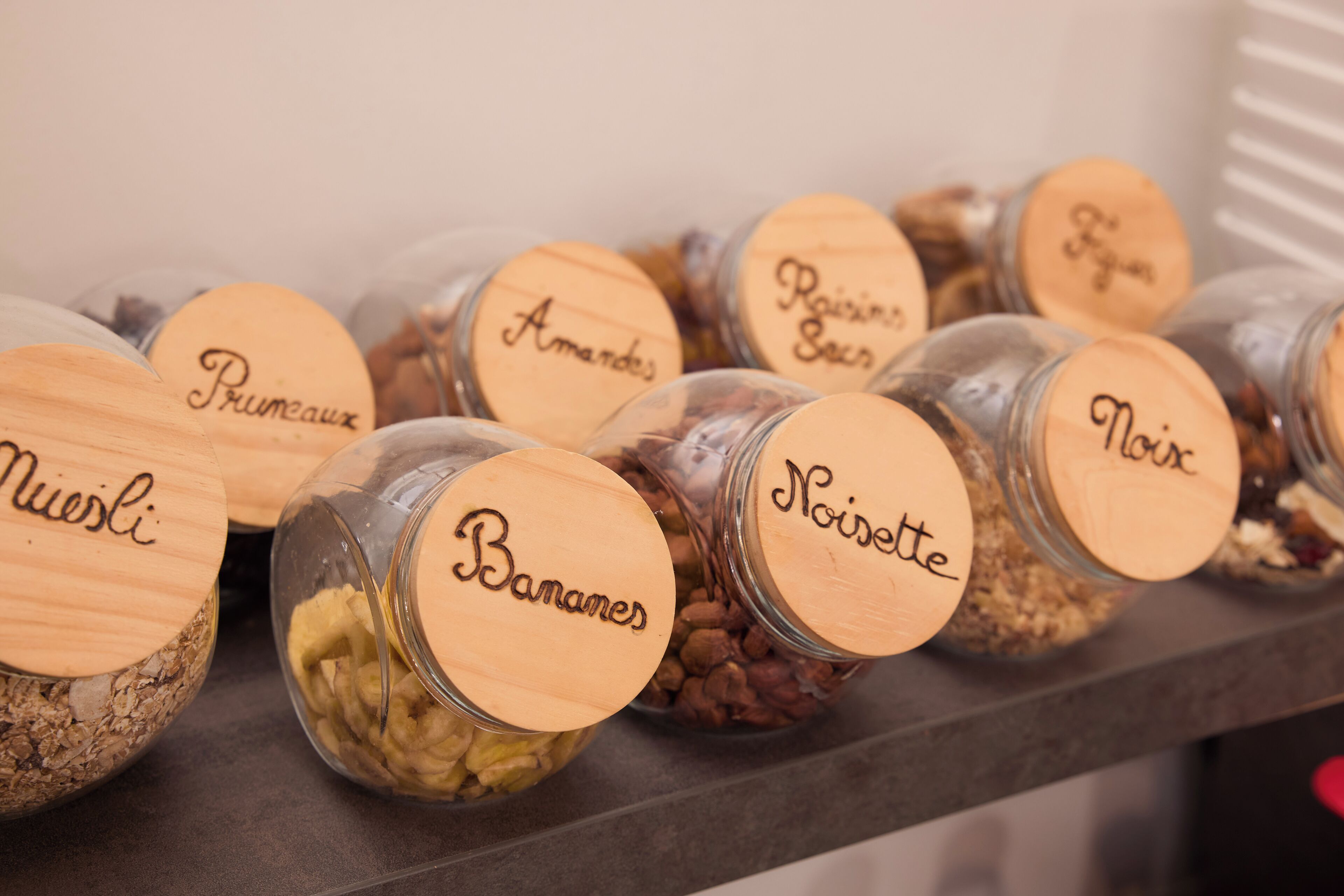 A shelf with jars labeled with names like "Pruneaux," "Amandes," and "Bananes."