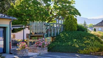 A residential property with a stone staircase leading to a wooden deck, surrounded by lush greenery and a clear sky.