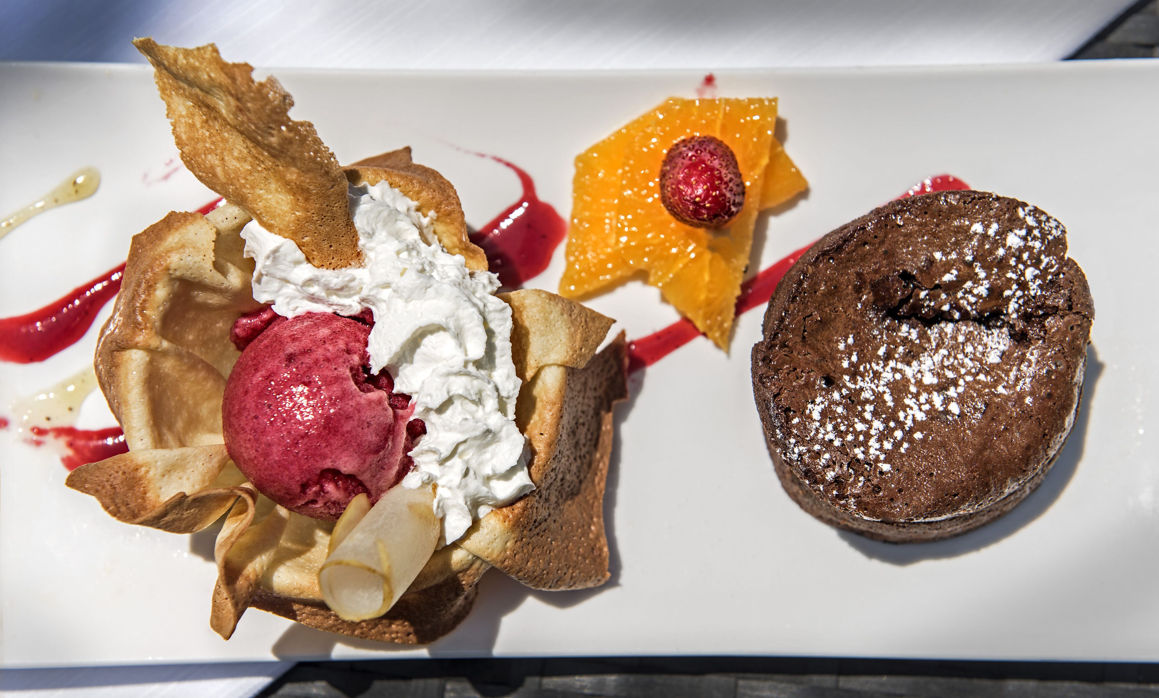 A dessert plate with a chocolate cake, a crepe with whipped cream and fruit, and a scoop of ice cream.