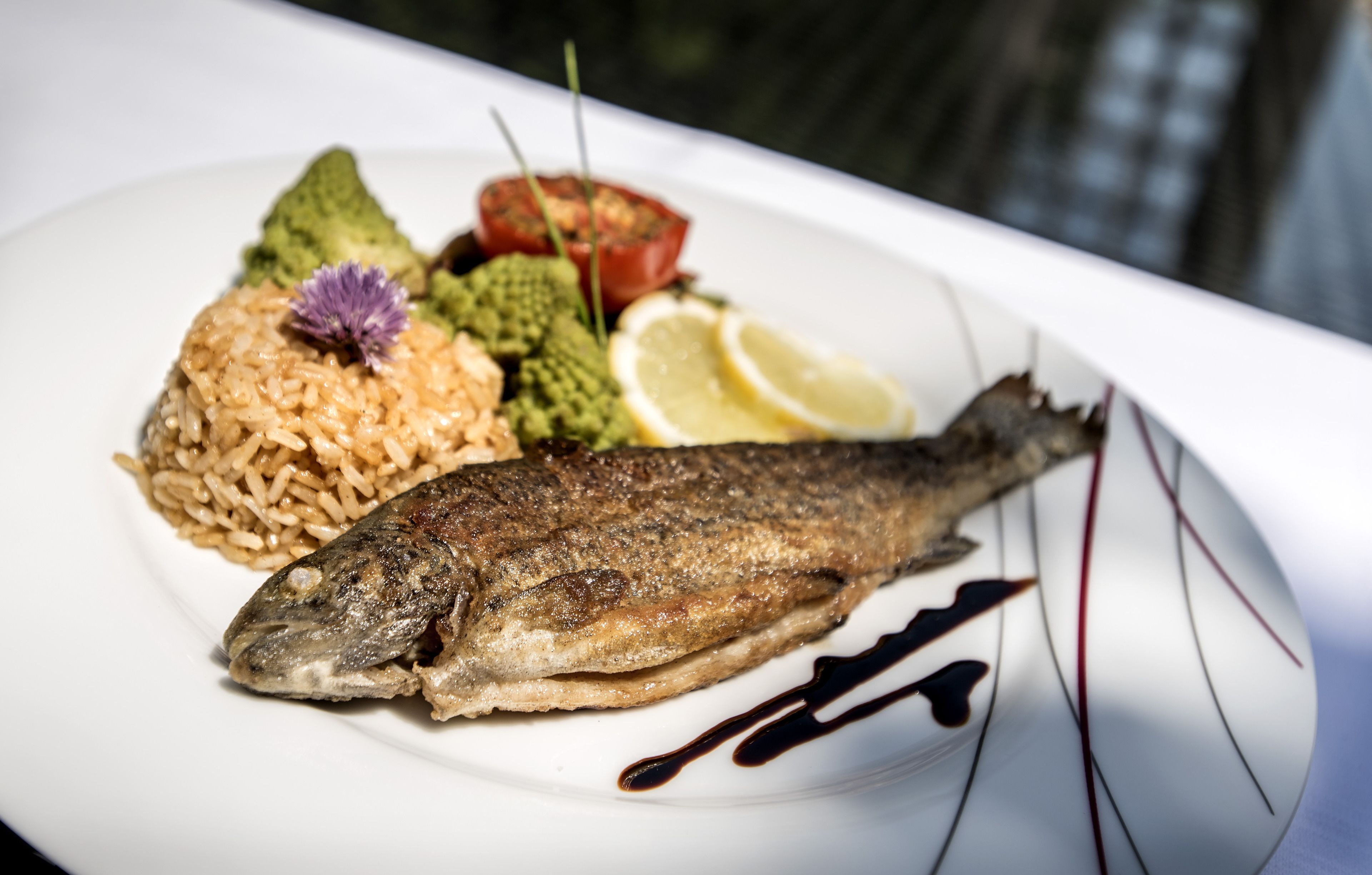 A plate with a whole fish, rice, avocado, tomato, lemon, and a decorative flower.