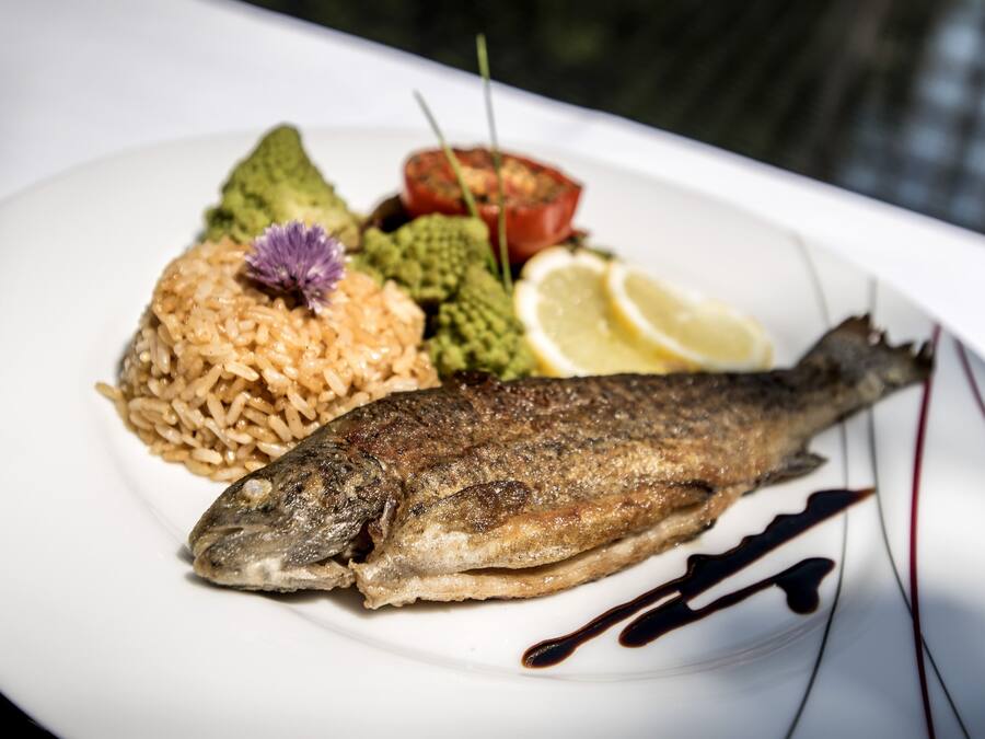 A plate with a whole fish, rice, avocado, tomato, lemon, and a decorative flower.