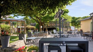 An outdoor patio area with tables and chairs, surrounded by potted plants and a pergola structure. - Hotel Le Calice du Gevaudan (Banassac)
