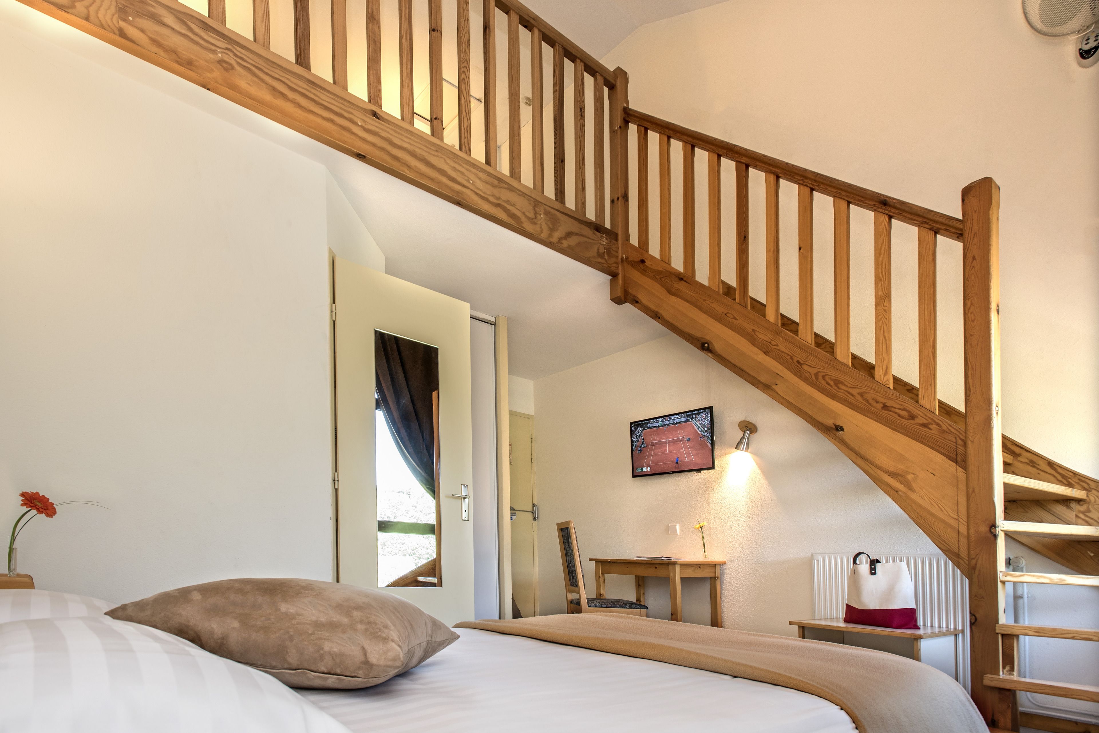 Une chambre avec un escalier en bois, un lit avec des oreillers, un bureau avec une chaise et un téléviseur fixé au mur.