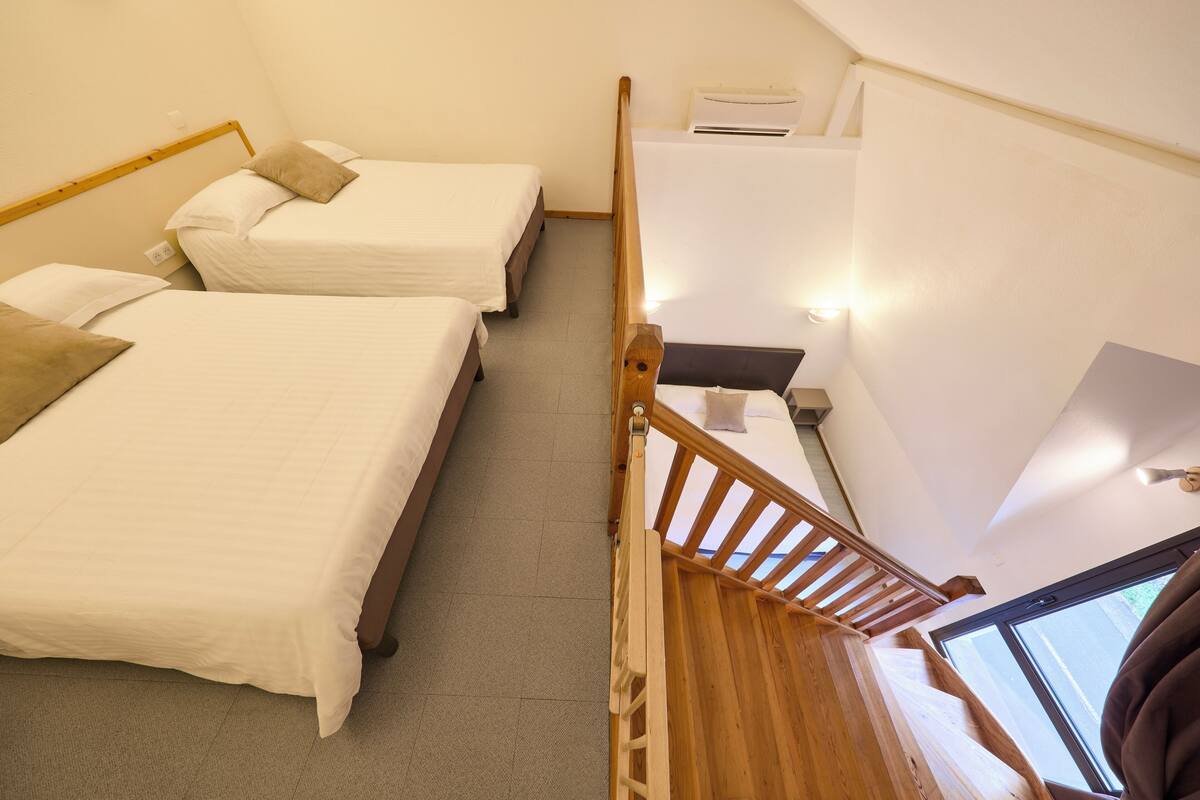 A room with two beds, a wooden staircase, and a window.