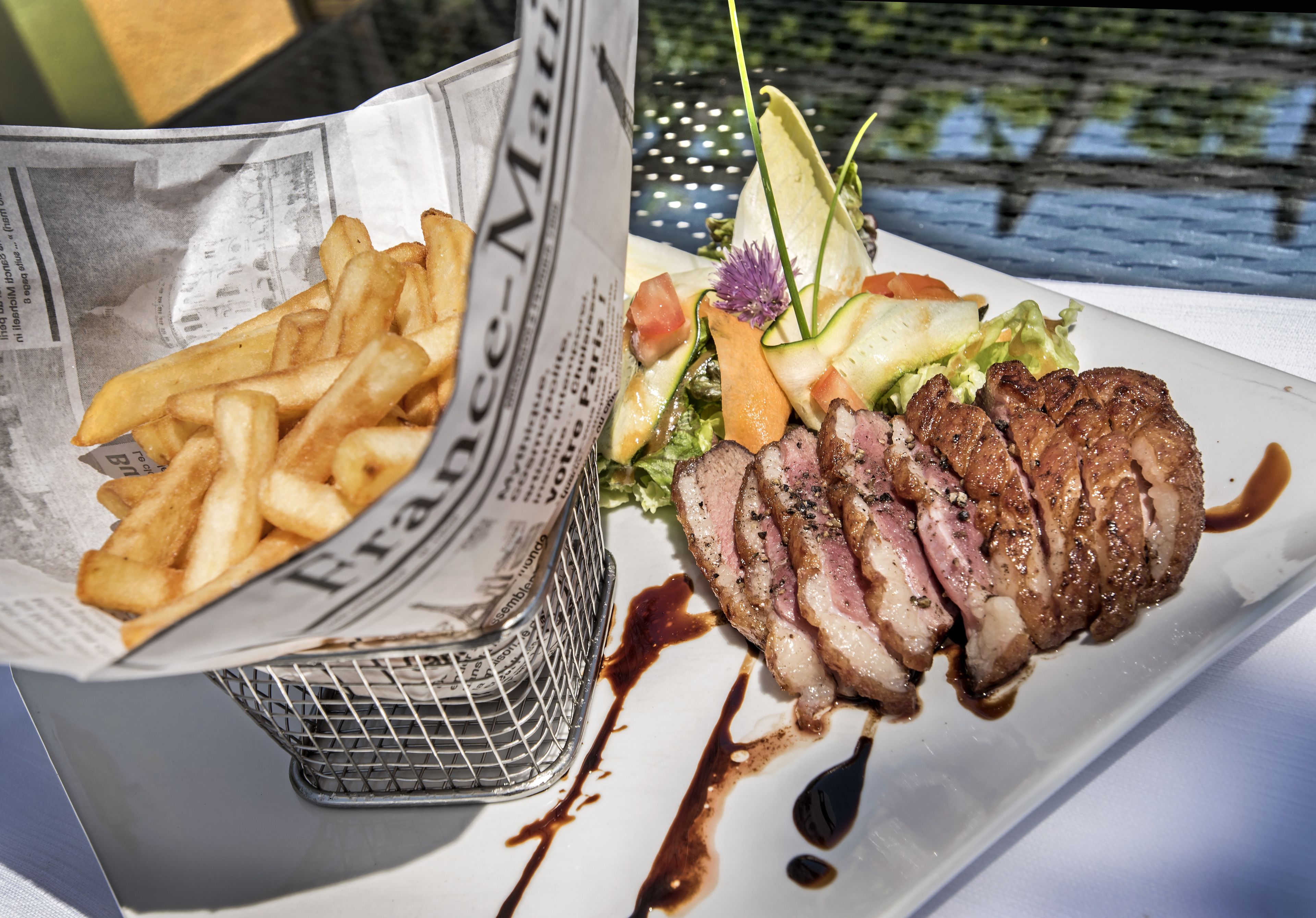 Une assiette de steak et de frites, garnie de légumes et de sauce.