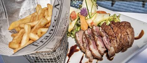Une assiette de steak et de frites, garnie de légumes et de sauce.