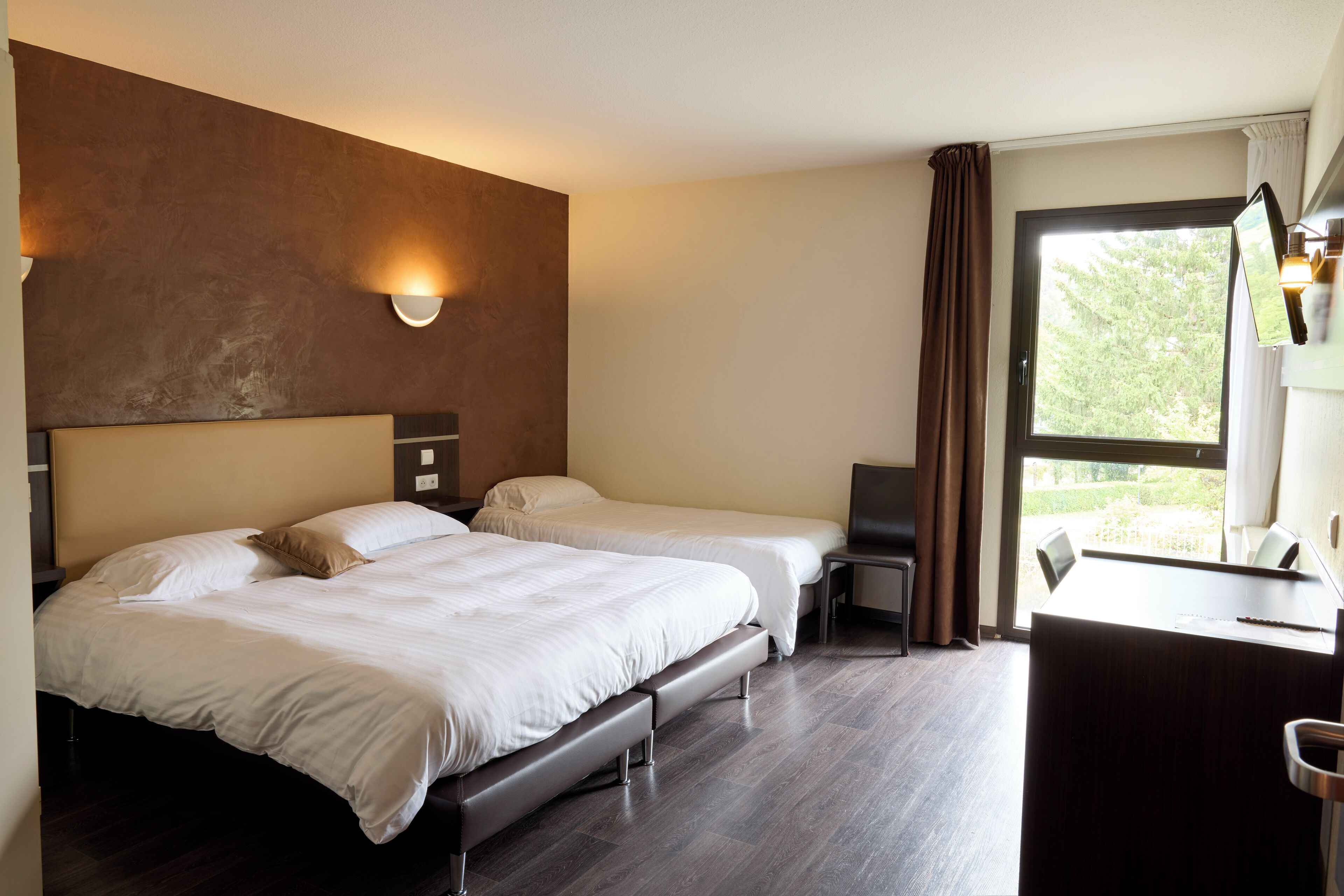Una habitación de hotel con dos camas, un escritorio y un ventanal grande.