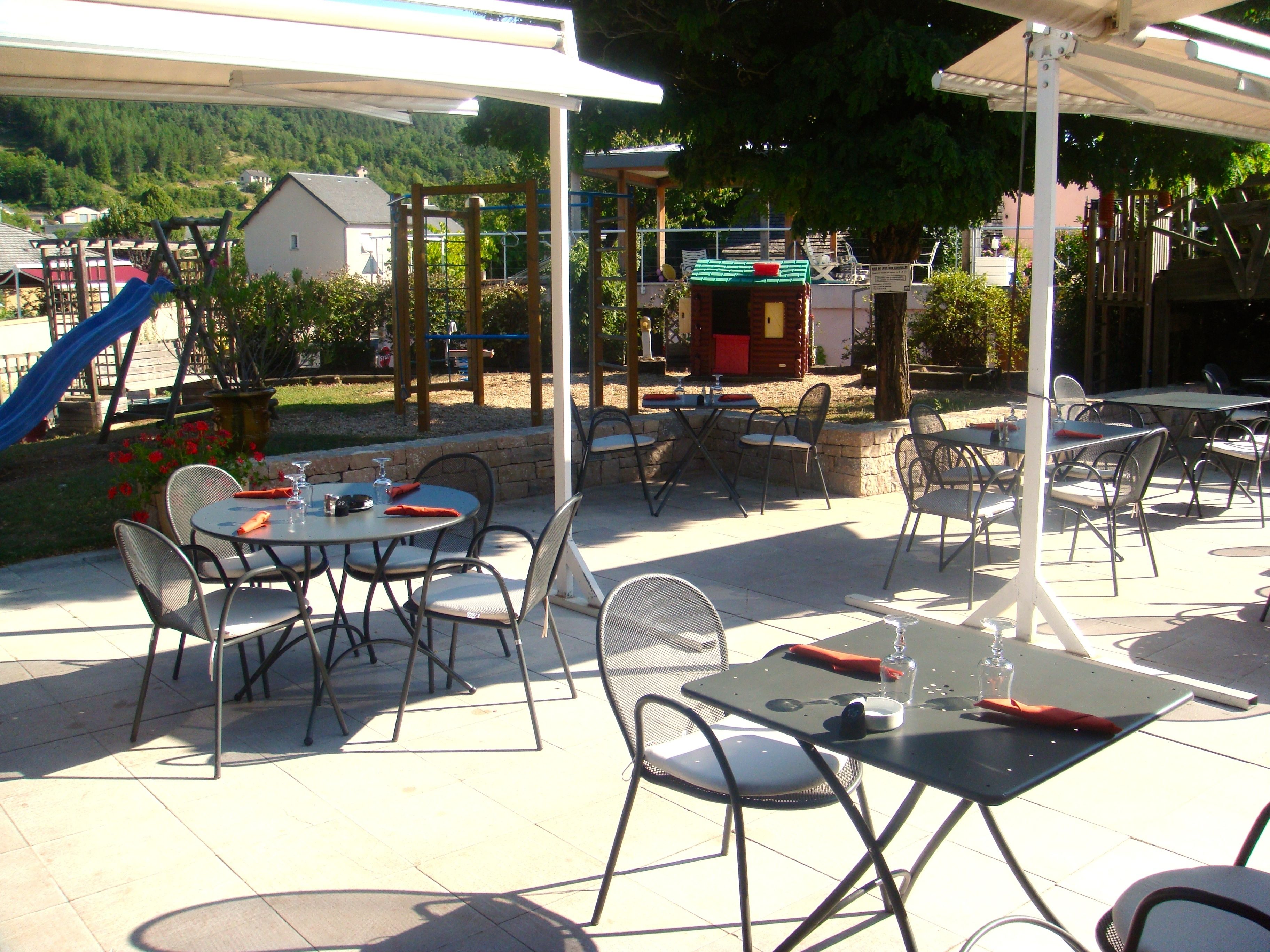 An outdoor patio area with tables and chairs, a children's play structure, and a small building with a green roof.
