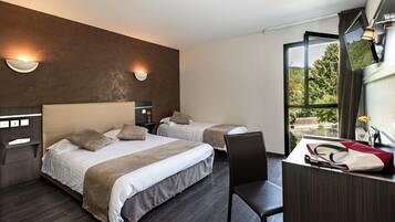 A modern hotel room with two beds, a desk, and a view of greenery.