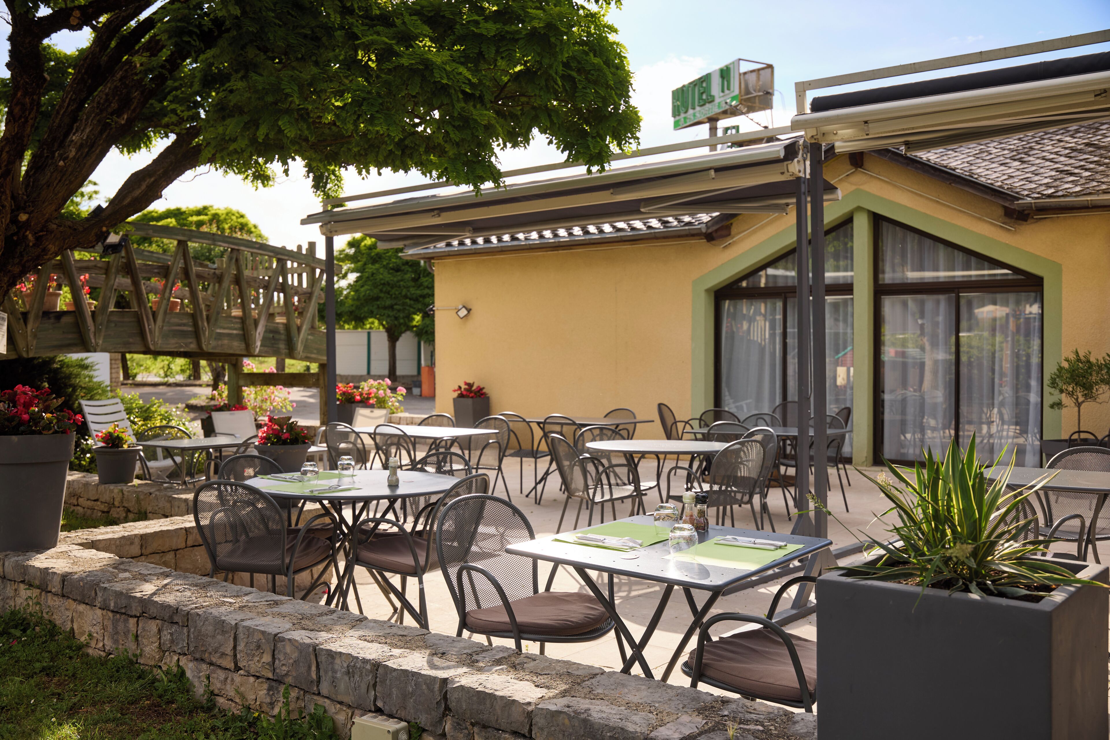 An outdoor patio with multiple tables and chairs, surrounded by potted plants and a stone wall.