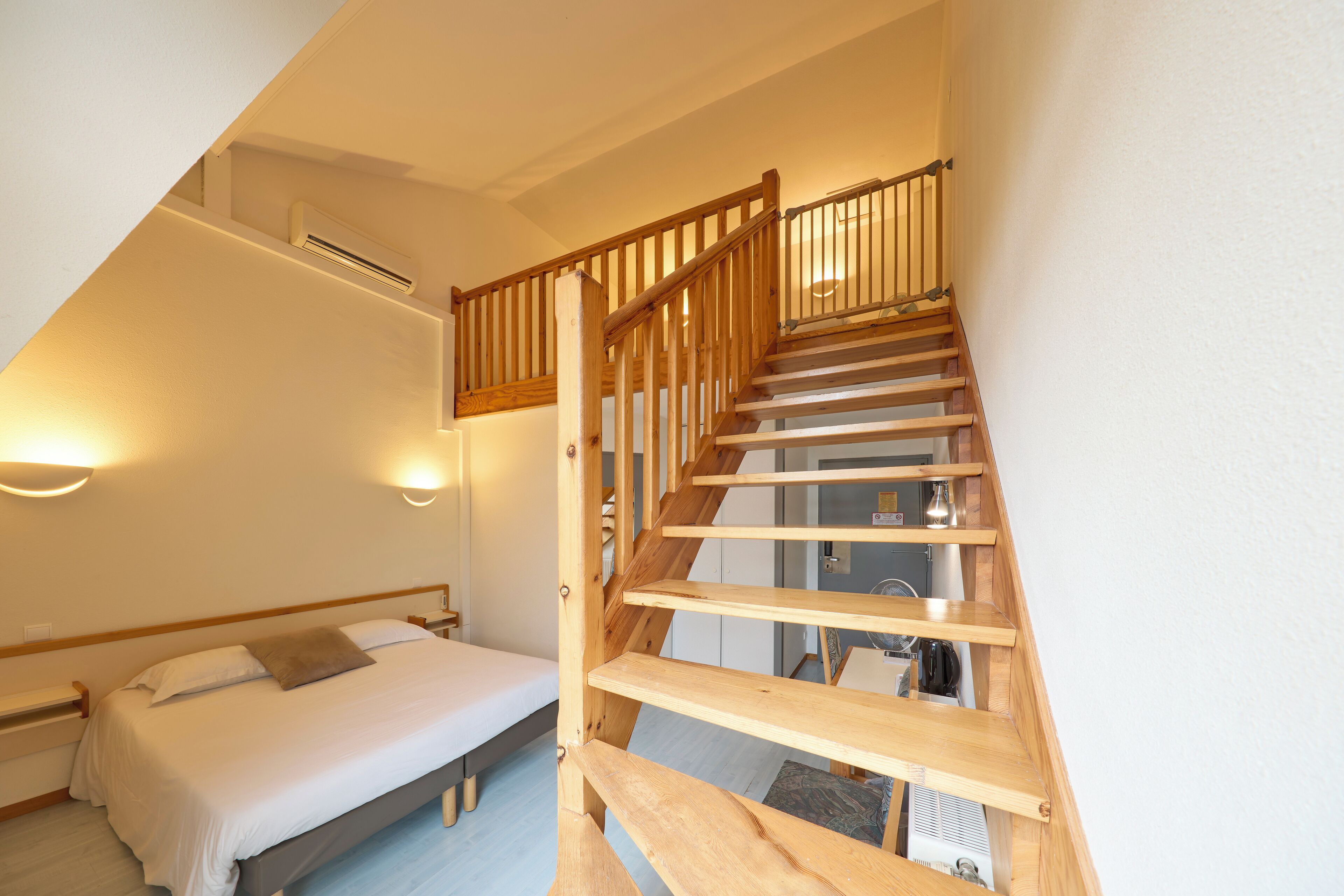 Un dormitorio con escalera de madera, una cama y una mesita de noche.