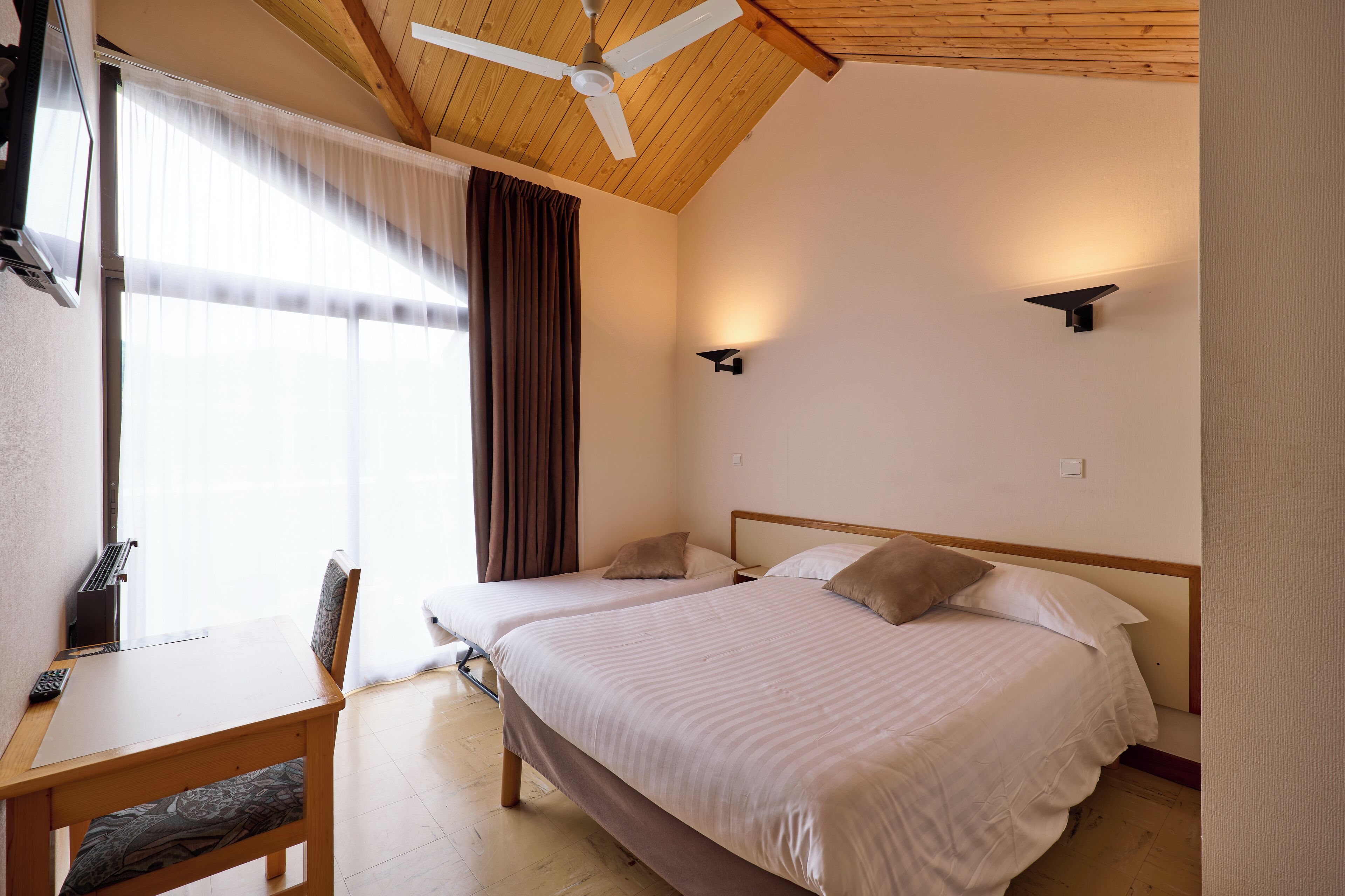 A bedroom with two beds, a desk, and a ceiling fan.