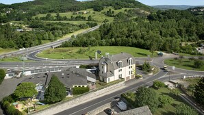 A multi-lane road with a roundabout, surrounded by residential houses and greenery. - Hotel Le Calice du Gevaudan (Banassac)