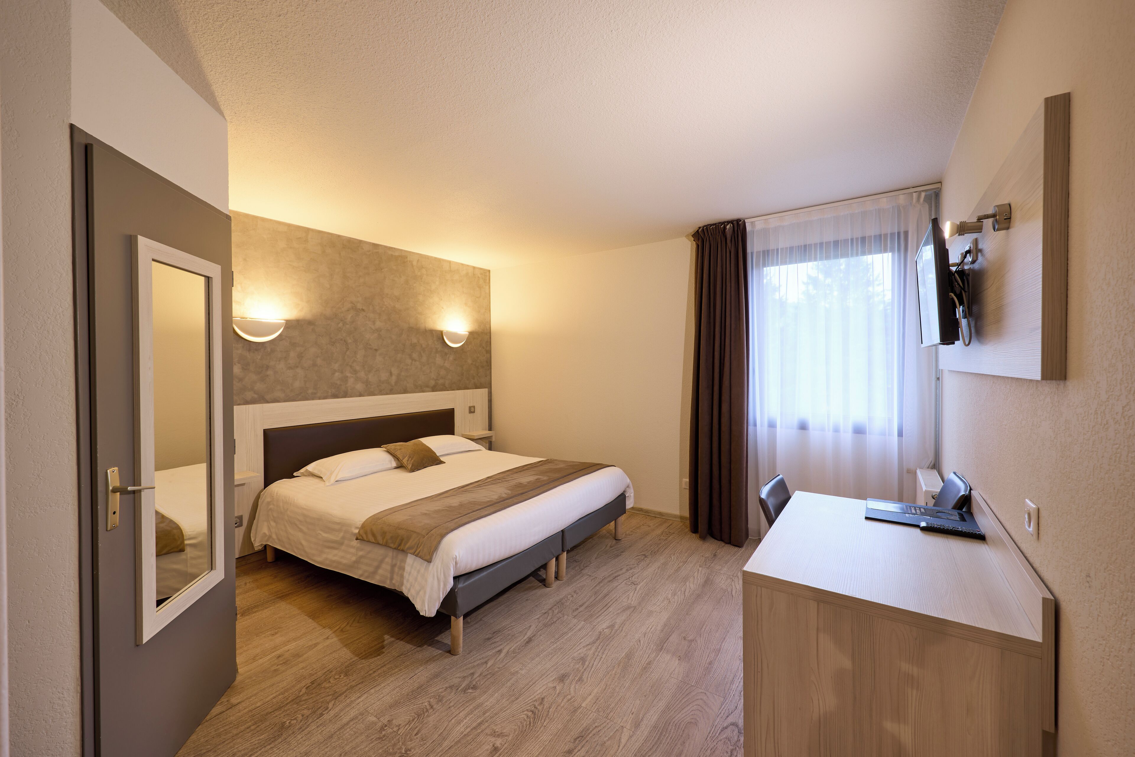A hotel room with a bed, bedside table, desk, and a mirror.